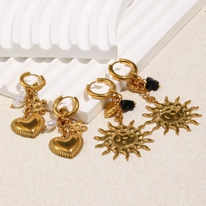 Detailed view of 18K gold plated heart and sun drop earrings with pearls on white texture