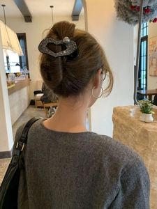 Fermaglio a cuore grigio glitterato con perla mostrato su una pettinatura a chignon