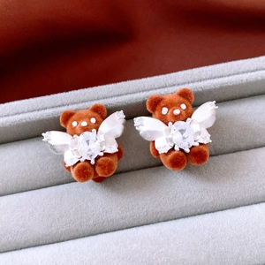 Macro detail of brown flocked bear earrings with silver wings and zircon on grey velvet box