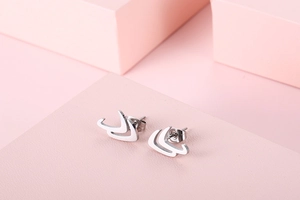 Macro shot of silver hollow V-shaped stud earrings on a textured pink surface