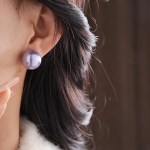 Close-up of a model wearing minimalist purple pearl earrings with golden plated posts