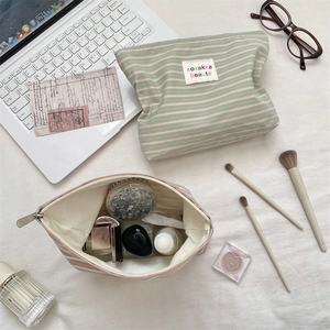 Flat lay of striped cosmetic bags with makeup brushes and skincare bottles on desk
