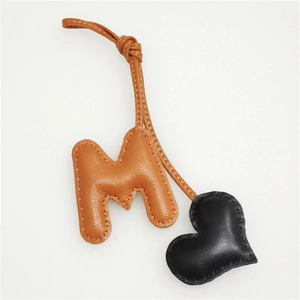 Detail of handmade leather bag charm with orange M letter and black heart shape