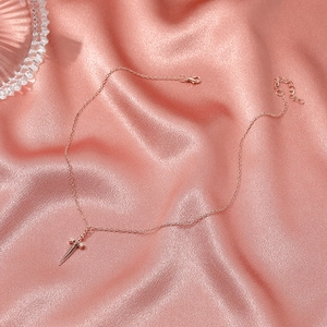 Dettaglio della collana con ciondolo a spada in oro rosa su sfondo di seta rosa