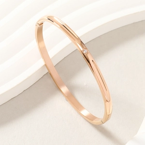 Close-up of rose gold stainless steel bracelet with diamond inlay on wave textured background