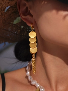 Gros plan de boucles d'oreilles à disques dorés avec longues chaînes à pompons sur un mannequin