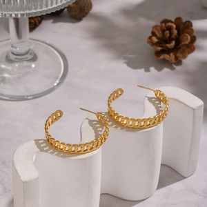 Gros plan de boucles d'oreilles créoles dorées à maillons cubains sur support blanc