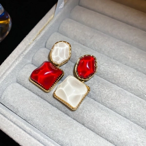 Makro-Detail von rot-weißen asymmetrischen Ohrsteckern mit goldenem Metallrahmenrand
