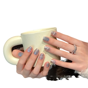 Handmade grey-blue cat eye press-on nails with glitter and rhinestones on a coffee cup