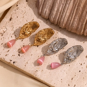 Detail of butterfly wing earrings with pink teardrop stones on textured sandstone surface