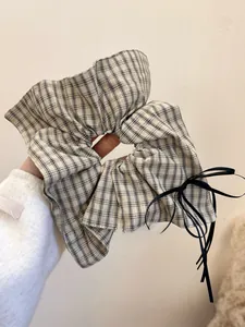 Detail of a beige plaid scrunchie with thin black ribbons and elegant bow design