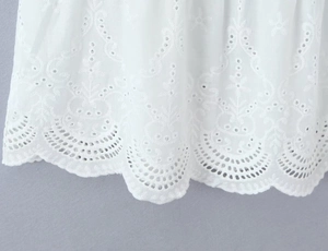 Detailed macro view of white cotton fabric featuring delicate floral eyelet embroidery