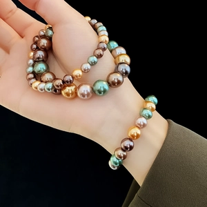 Détail de perles multicolores vert foncé et or champagne sur une main élégante