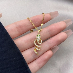 Detailed close-up of 18K gold snake pendant necklace with white zircon and green eyes