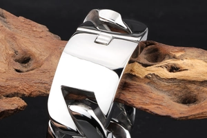 Polished silver cuban chain bracelet for men displayed on a natural wood log base
