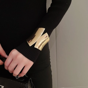 Polished gold wide irregular metal cuff bracelet worn over a black sweater sleeve