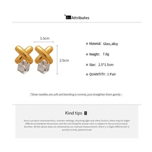 Detailed view of gold X-shaped earrings with glass stones and silver needles specs