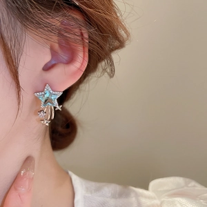 Detailed view of luxury silver star earrings with blue zircon and tassels on a female model