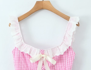 Detail of pink plaid top featuring white lace ruffle trim and satin ribbon bow details