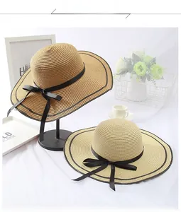 Detail view of straw sun hats with black ribbon bow and trim on a lifestyle background