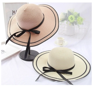 Detail of two foldable straw sun hats with black bow accents and stitched brims