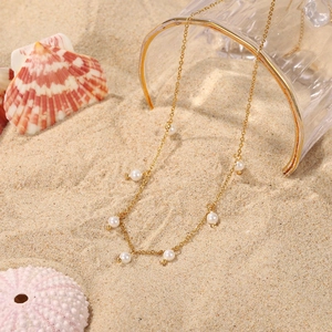 Detail shot of 18K gold stainless steel pearl necklace on sand with shells and glass