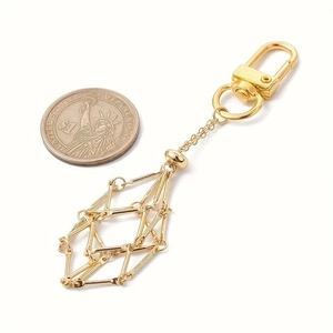 Detail of a geometric gold hollow pendant keychain with a lobster clasp and coin for scale