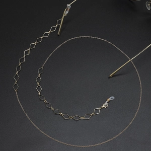 Detail of golden metal eyewear chain with geometric diamond charms on black background