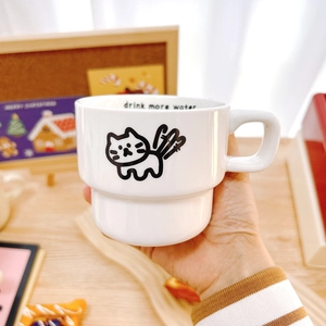 Minimalist stackable ceramic cat mug with 'drink more water' text in a cozy setting