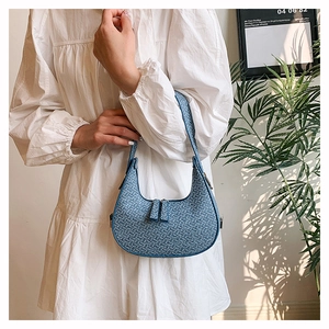 Detailed blue woven crescent bag being held by a model in a stylish white dress