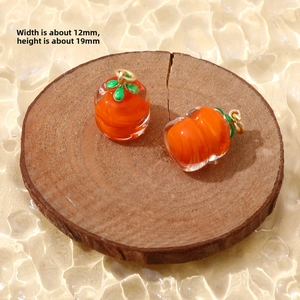 Detailed view of handmade persimmon glass charms with orange body and green leaf accents