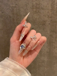 Detail showing elegant silver bow nail charms with oval rhinestones on almond shaped nails