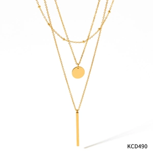 Detail einer goldenen Doppelkette mit rundem Anhänger und langem Quastenstab auf weißem Grund