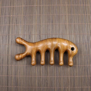 Handcrafted sandalwood meridian massage comb with five teeth on a bamboo mat background