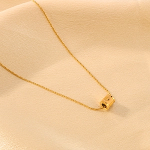 Elegant gold cylinder pendant necklace with heart cutout on soft beige silk background