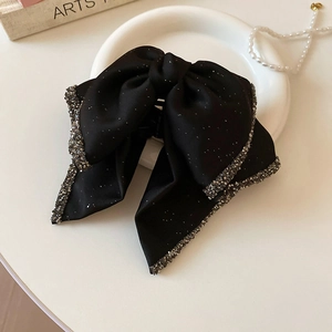 Top view of a black satin bow hair claw with sparkling rhinestones on a decorative tray
