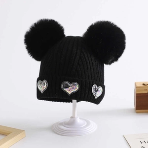 Close-up of black knit baby beanie featuring dual pom-poms and sequin heart details