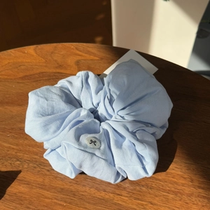 Detail of light blue oversized fabric scrunchie with transparent bow button on a wooden table