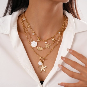 Close-up of three-layer gold necklace featuring starfish, shell charms and pearl beads
