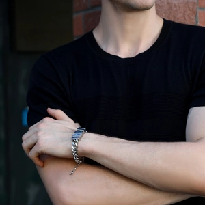 Close-up of silver Cuban link bracelet with square charms worn on a man's wrist