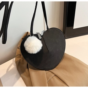 Detail einer schwarzen herzförmigen Handtasche mit weißem Pelzanhänger auf Blazer