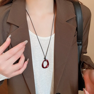 Gros plan d'un collier pendentif rouge foncé sur une tenue avec un blazer marron
