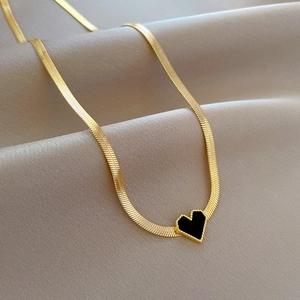 Detail of gold snake chain necklace featuring a black heart pendant with beaded edges