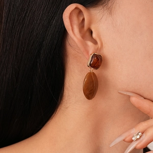 Close-up of caramel resin oval earrings with gold trim worn by a model in a retro style