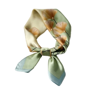 Elegant silk scarf featuring green and gold ginkgo leaf patterns on a white background