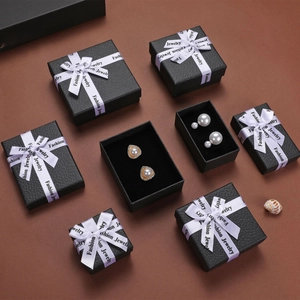 Black textured jewelry gift boxes with white ribbons and pearl earrings inside