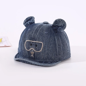 Détail d'une casquette bébé en denim bleu avec oreilles d'ours et broderie sur bord souple