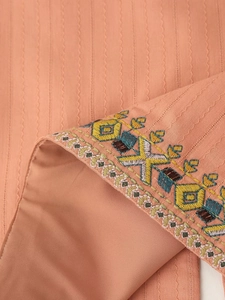 Close-up detail of ethnic embroidery on orange-pink vest fabric with wave textures
