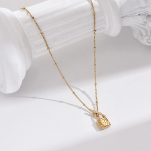 Close-up of golden lock pendant necklace with beaded chain on a white plaster column