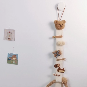 Beige fabric hanging hair clip organizer featuring a plush bear head and various clips